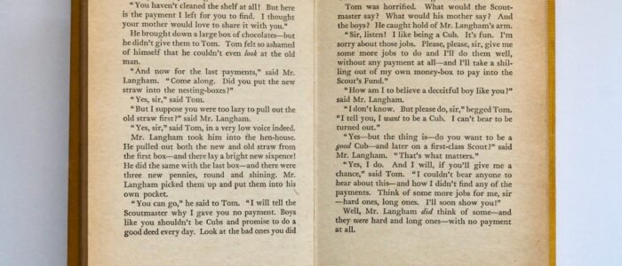 Vintage book opened to pages 76-77, displaying classic literature text in soft lighting.